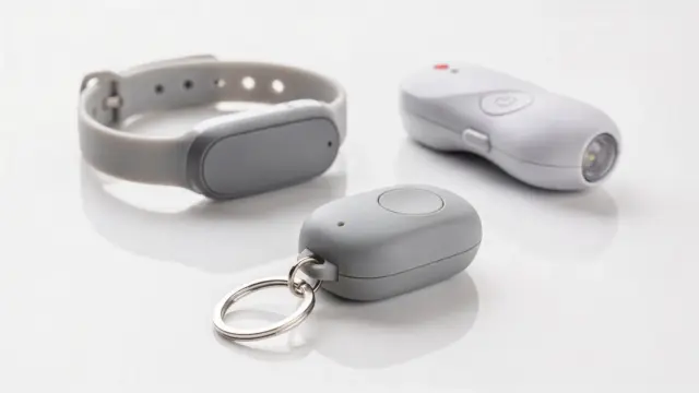 Persönliche Alarmgeräte für Selbstschutz: Schlüsselanhänger-Alarm, Wearable und Handgerät auf weißem Hintergrund